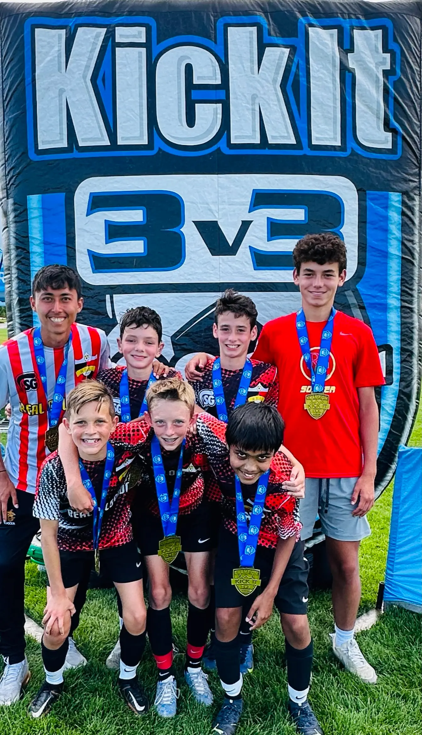 Real Colorado Academy team in red and black kits with gold medals in front of Kick It 3v3 banner July 2023